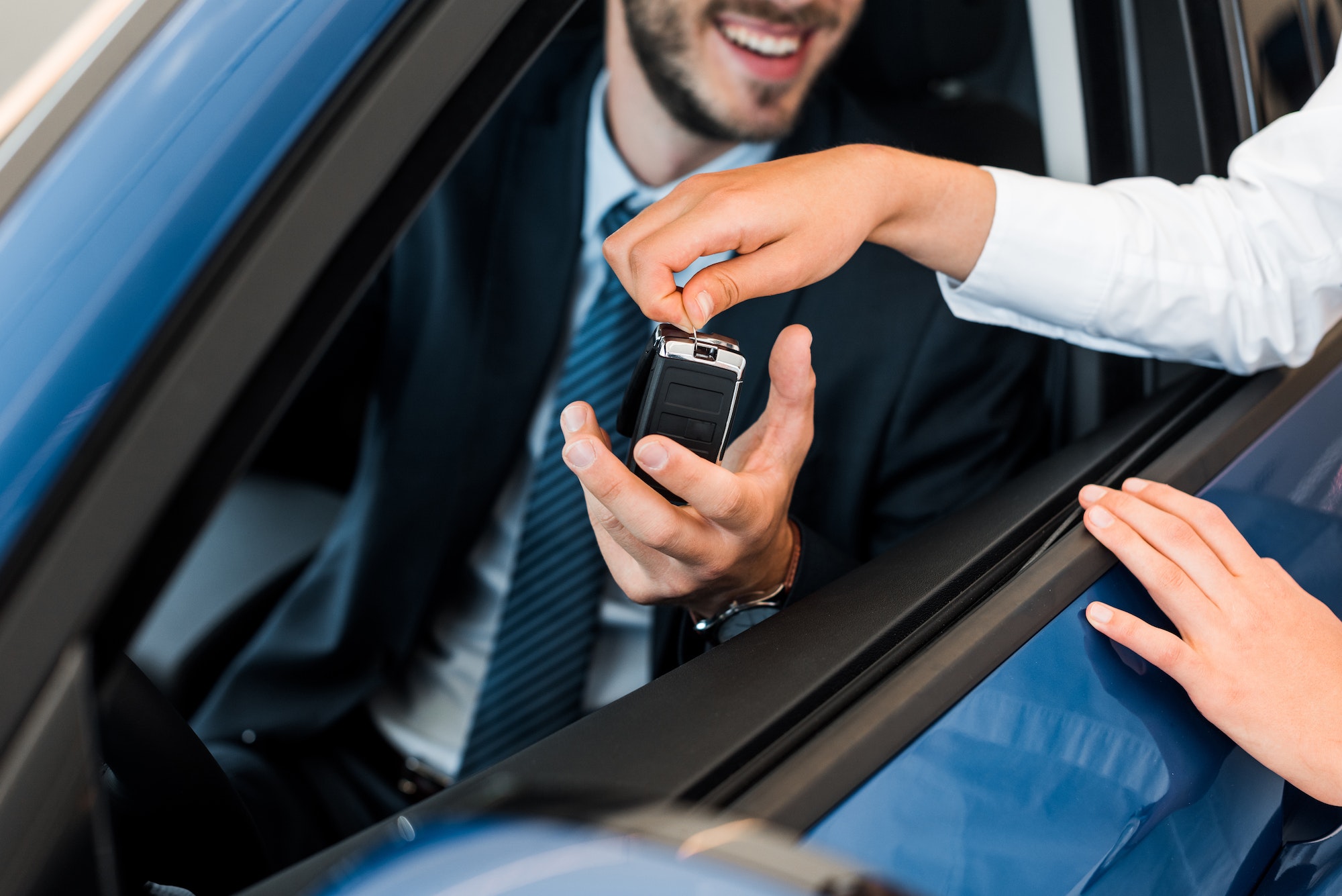 cropped view of car dealer giving car key to bearded man